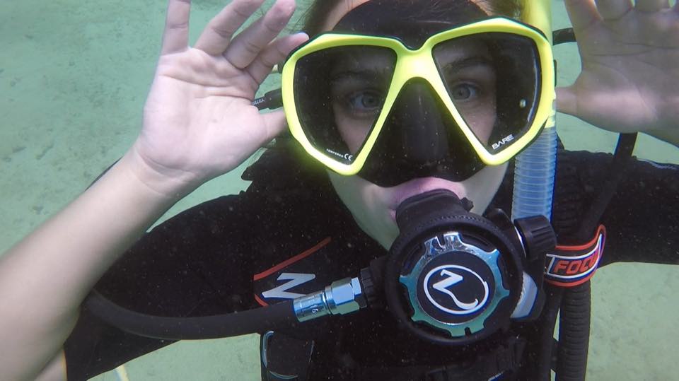A first-time diver waving at the camera underwater