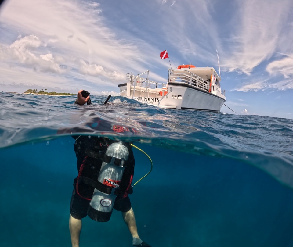 Over-under view of a diver below the surface and the boat Four Points above